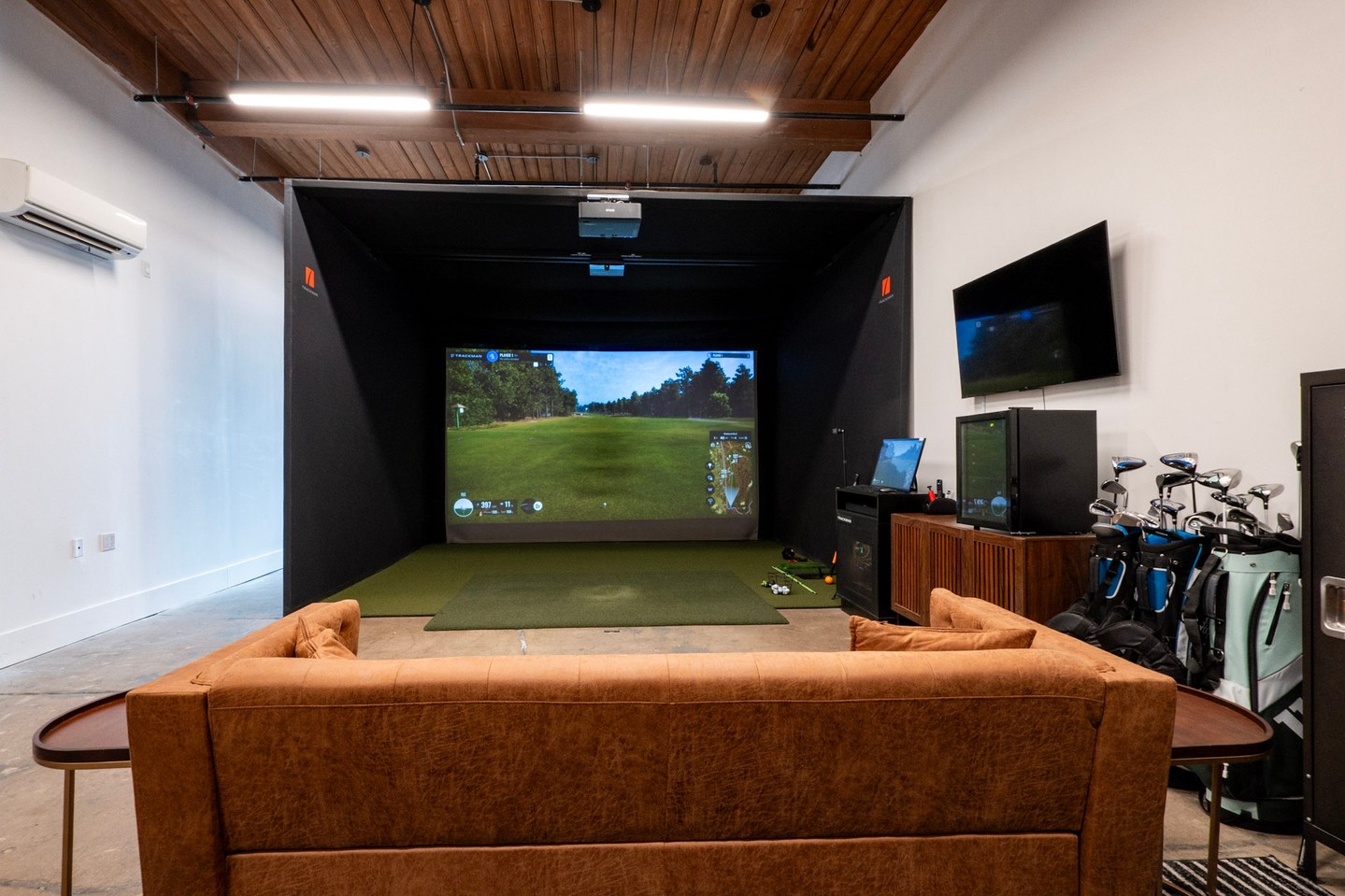 Golf simulator bay with leather couch and TrackMan screen at Gowanus Golf Club